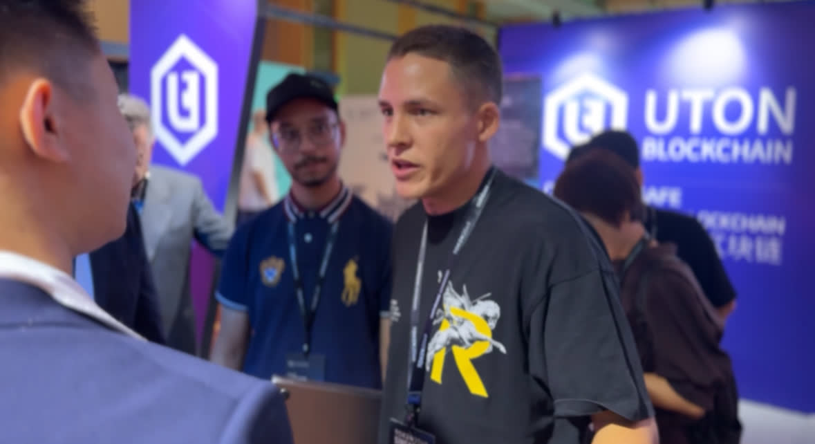 Two people in conversation beside a conference stand, others walking past behind them.